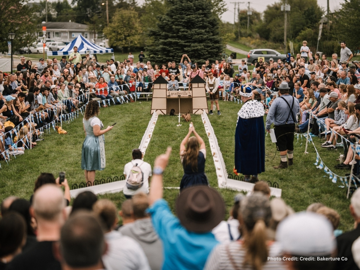 Crowd watching the famous Wiener Dog Races at Lovettsville Oktoberfest in Virginia, with a dachshund racing down the track surrounded by spectators in traditional German attire